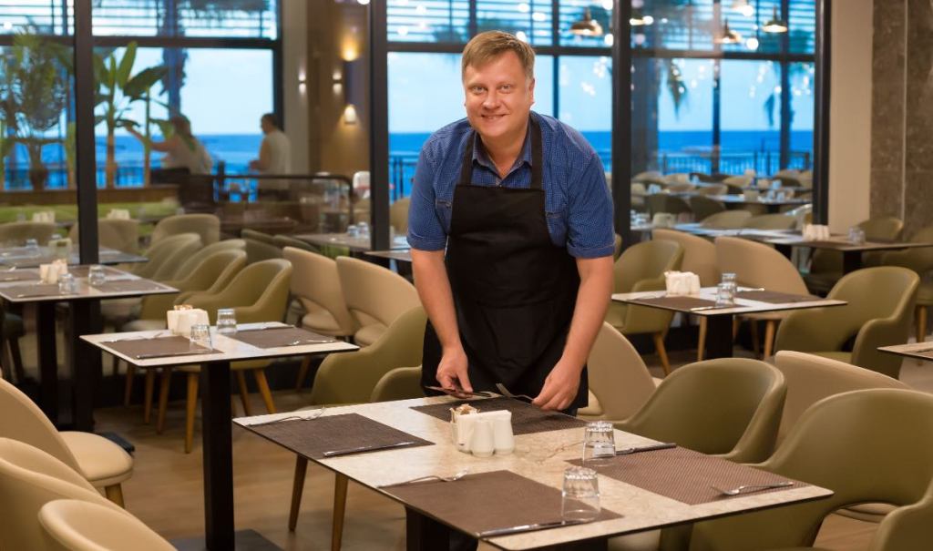 Ein lächelnder Kellner deckt einen Tisch in einem Restaurant.