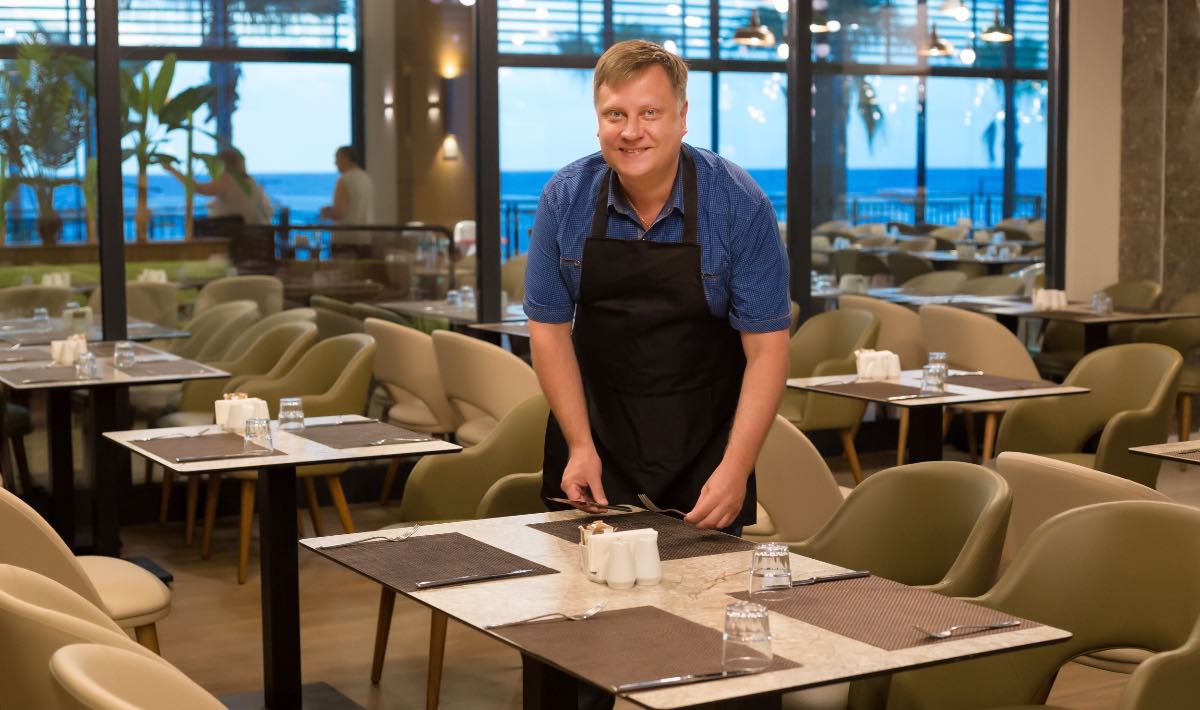 Ein lächelnder Kellner deckt einen Tisch in einem Restaurant.