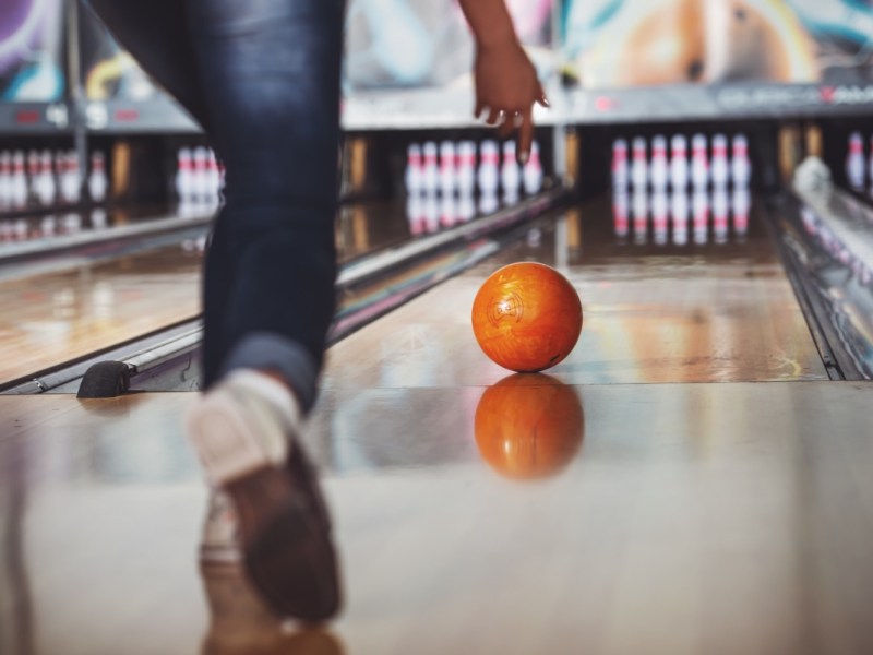 Eine Frau beim Bowling wirft eine Bowlingkugel.