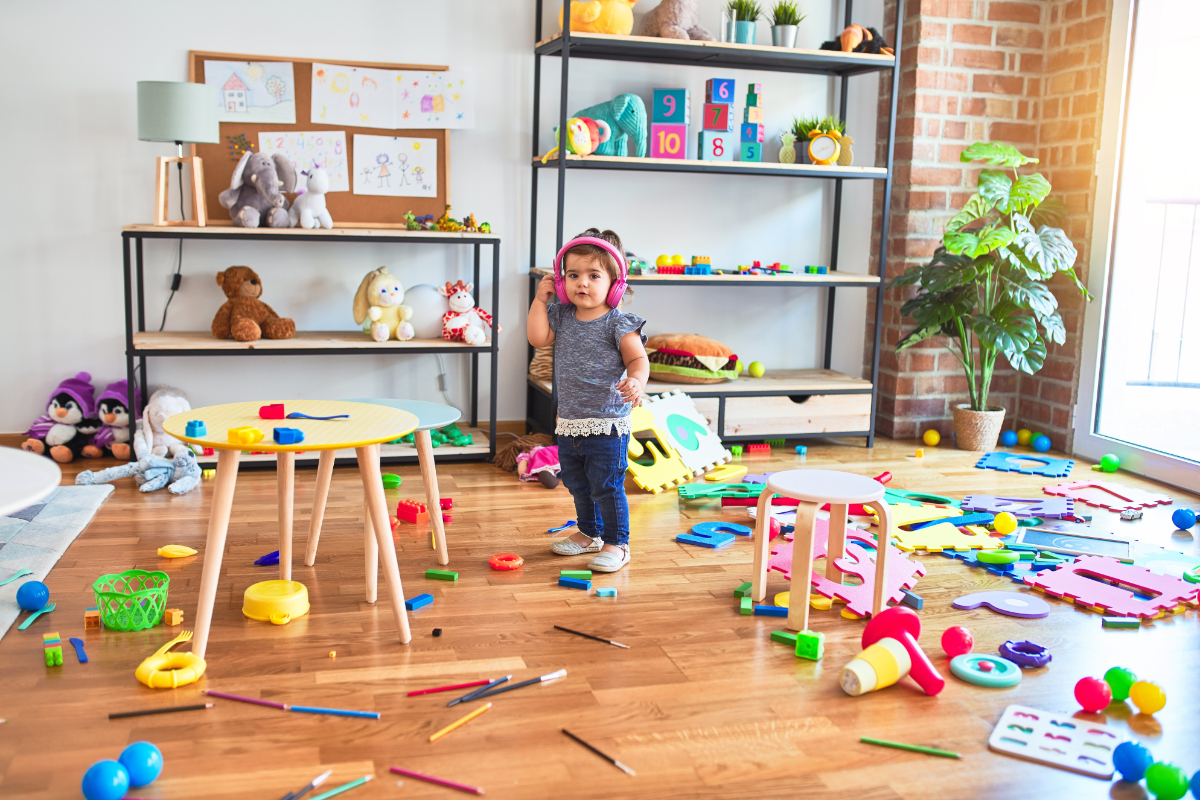 Ein kleines Mädchen steht in einem unordentlichen Kinderzimmer.