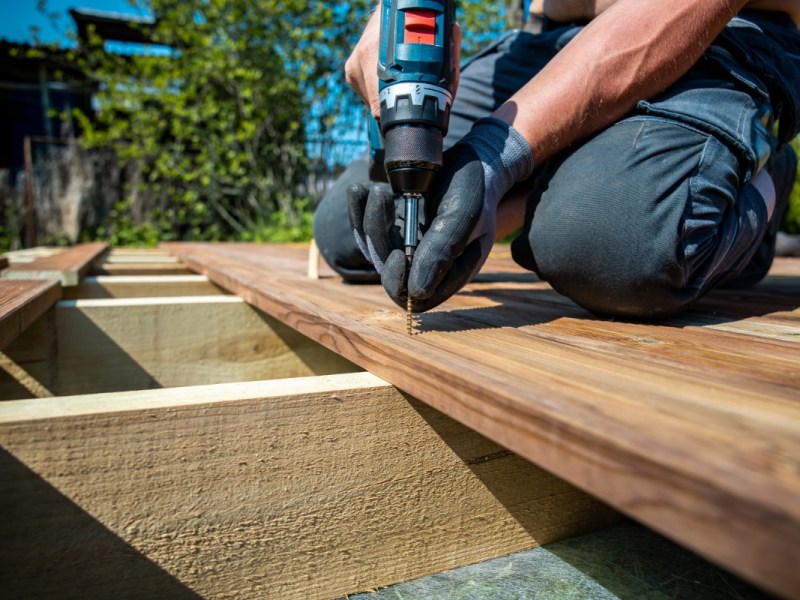 Ein Handwerker bohrt die Bretter einer Veranda fest.