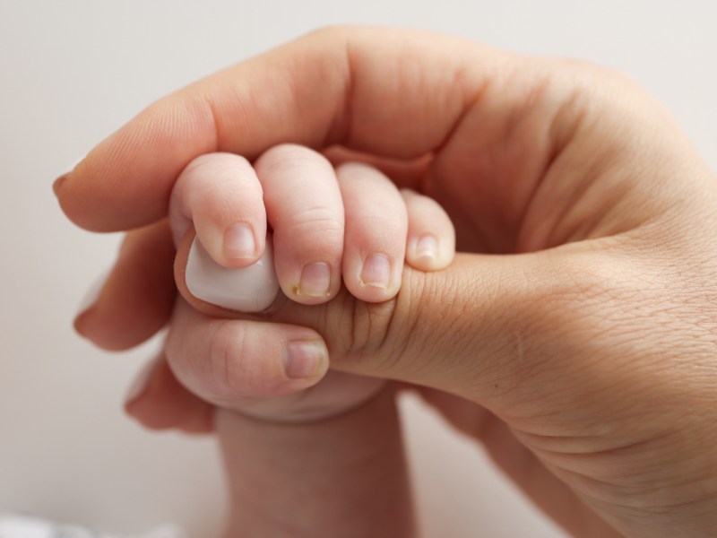 Ein Baby umfasst mit der Hand den Daumen seines Vaters.