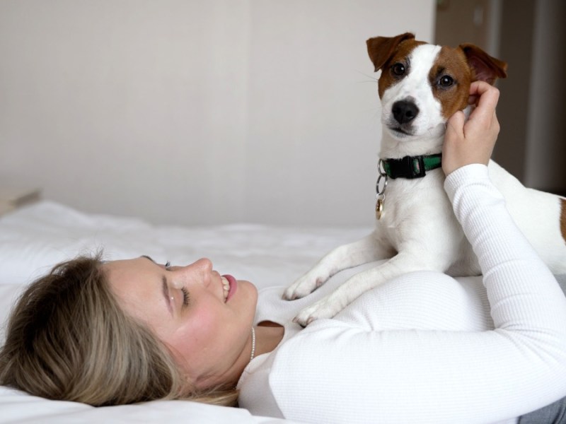 Eine Frau kuschelt mit einem Hund auf einem Hotel-Bett.