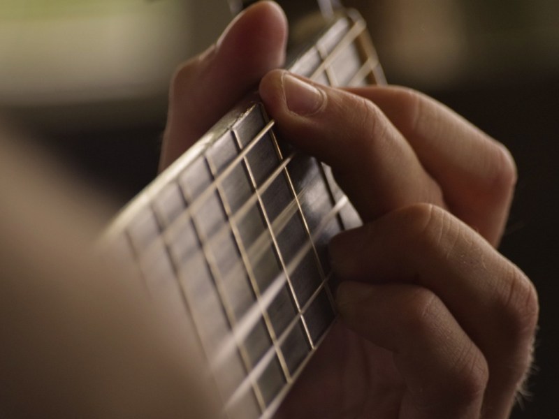 Ein Foto von einer Hand, die einen Akkord auf einer Gitarre greift.